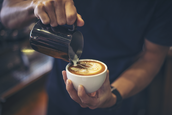 Nahaufnahme der Hände eines Baristas, der einen Latte macht