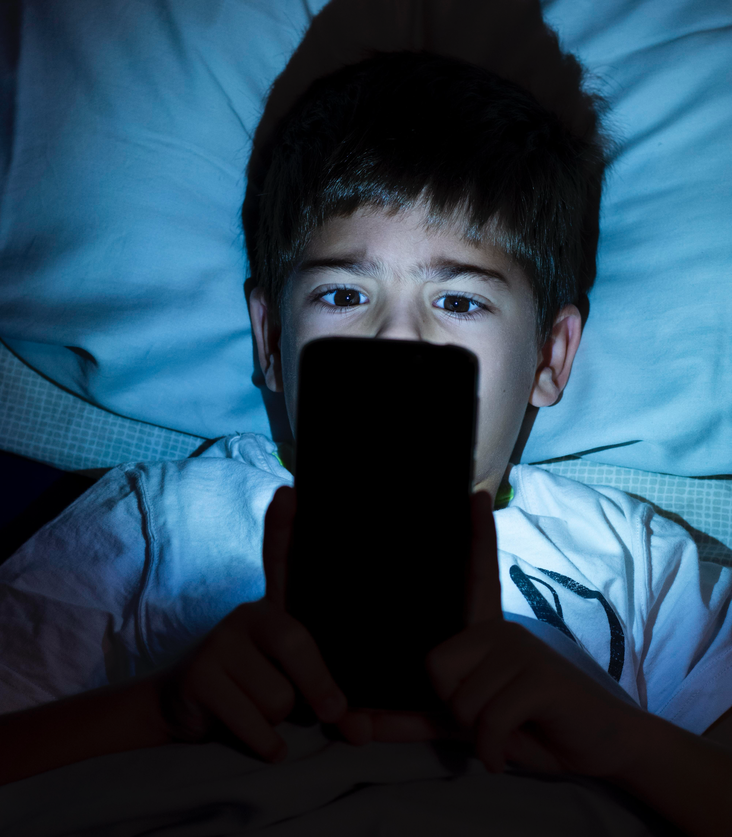 Close-up kid on the phone, in bed, at night