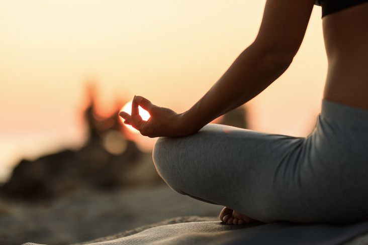 Woman meditating in lotus position at sunset